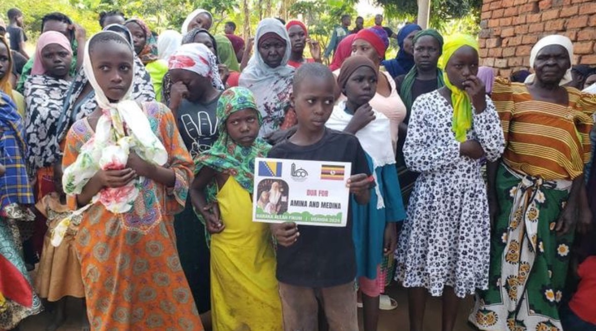 A group of women and children standing together, holding a sign calling for help, symbolizing the urgent need for donations to support families in crisis.
